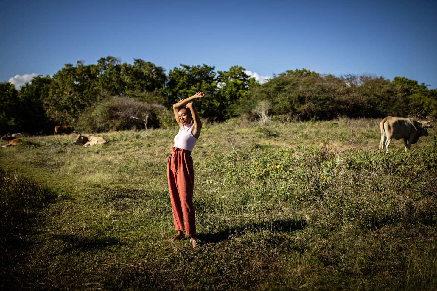 Axelle Célina, assise en tailleur vert sauge, regard doux, détail or et plum, lumière naturelle tropicale de Guadeloupe